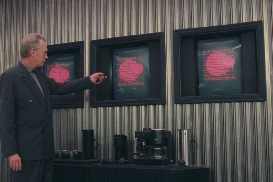 <p>Vilos Cohaagen thumbing the control of a monitor, one of three displaying the Federal Colonies logo. Again, the lines on the corrugated steel walls complement the repeating lines seen in the logo design.</p>