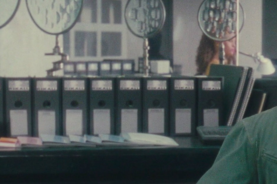 <p><strong>Figure 2.6</strong> Lining the shelving behind Quaid, we see binders with the Rekall logo on their spines. We also see these in the lab, where Quaid is to receive his memory implant.</p>