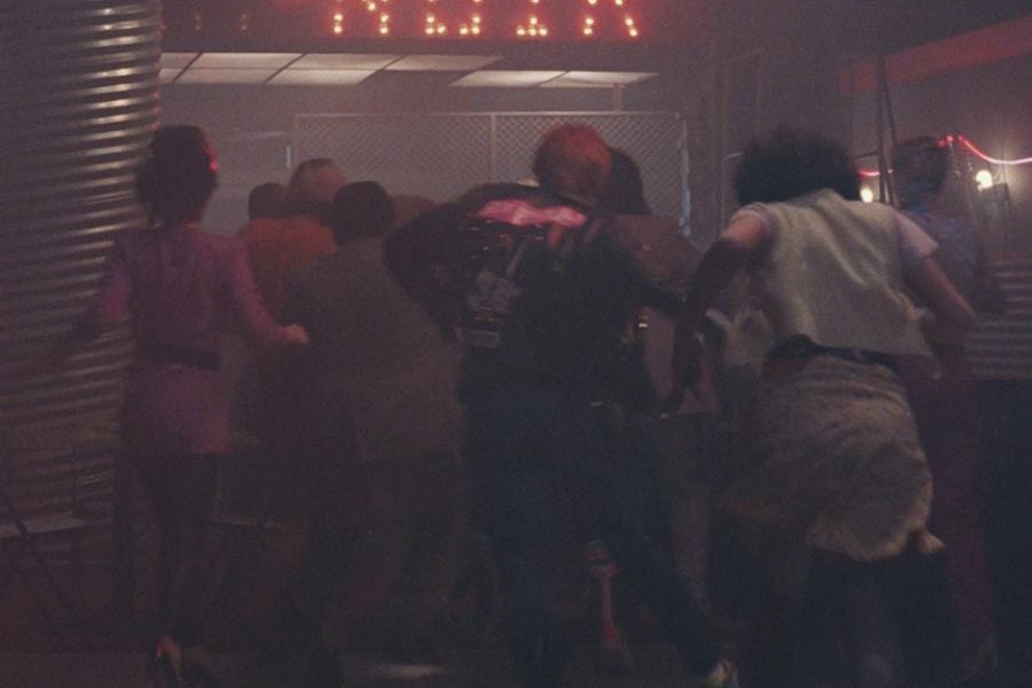 <p><strong>Figure 1.3</strong> The Version B interior light bulb signage also appears near the exit, and is partially visible above as patrons flee the carnage.</p>
